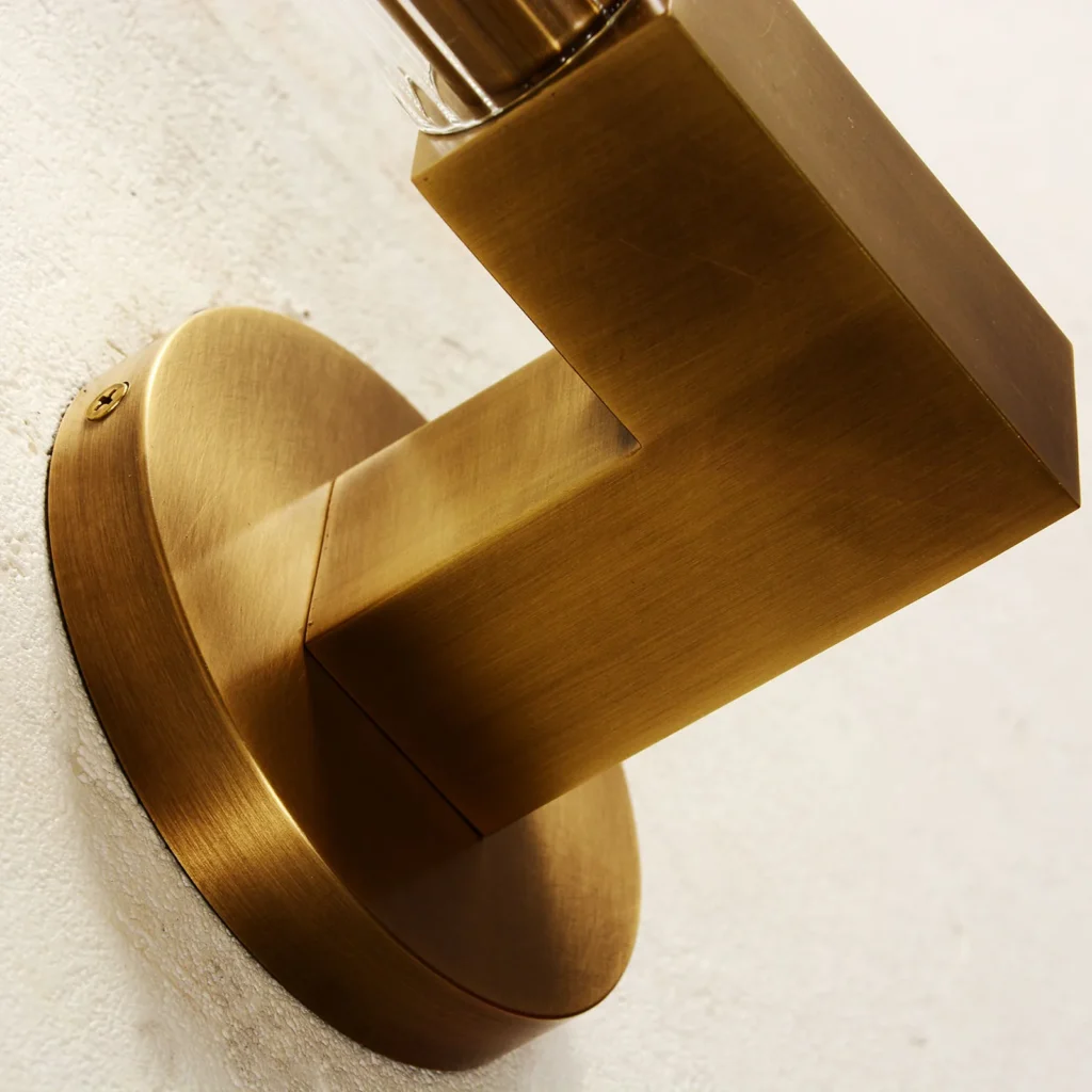Brass tube wall sconce close-up showing the brushed brass arm and round wall plate